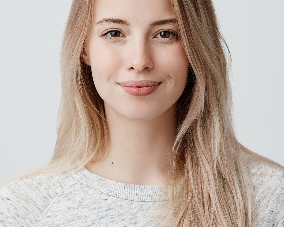 Head-and-shoulders portrait of a smiling young woman with long blonde hair in a light gray sweater against a neutral background