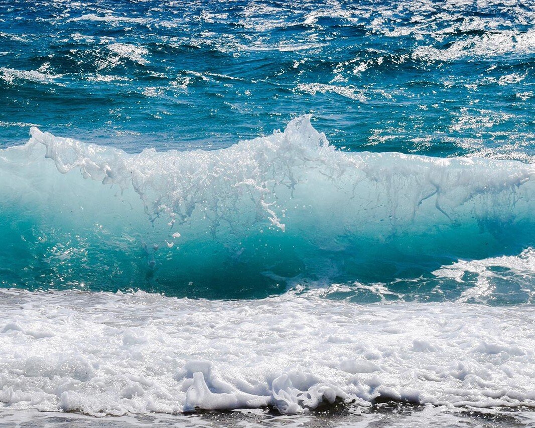 Turquoise ocean wave curling and crashing onto a foamy white surf near the beach.