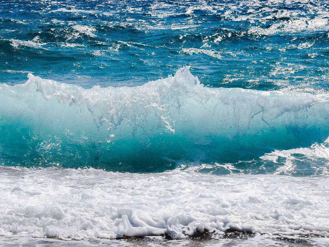 Turquoise ocean wave curling and crashing onto a foamy white surf near the beach.
