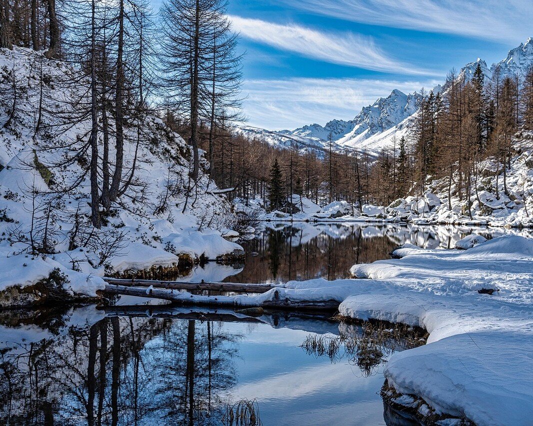 Snowy mountain landscape with a calm river reflecting trees and blue sky