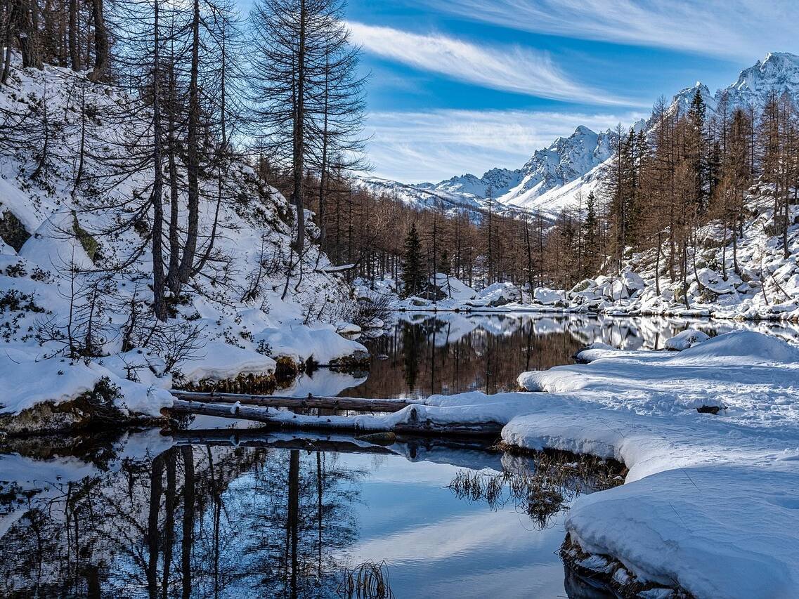 Snowy mountain landscape with a calm river reflecting trees and blue sky